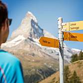 Wanderer betrachtet Wegweiser mit Zielen in den Alpen.