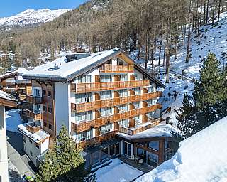 Mehrstöckiges Hotel mit Holzbalustraden in verschneiter Berglandschaft und Nadelbäumen