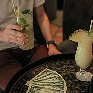 Ein Mann hält einen Cocktail, während Spielgeld auf dem Tisch liegt.