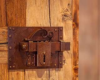 Detailaufnahme eines rustikalen Holztores mit einem metallenen Schloss.