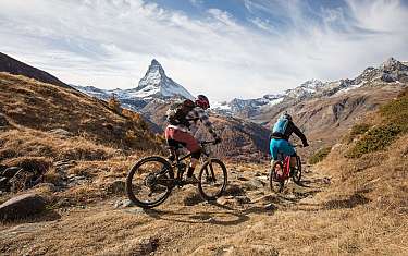 Deux vététistes traversent un paysage alpin avec le Cervin en arrière-plan.