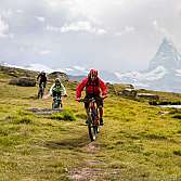 Drei Mountainbiker fahren auf einem Pfad mit Bergblick.