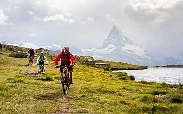 Trois vététistes roulent le long d'un lac avec vue sur les montagnes.