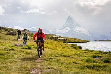 Drei Mountainbiker fahren auf einem Pfad mit Bergblick.