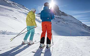 Deux skieurs regardent les montagnes sous la lumière du soleil.