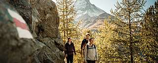 Trois personnes marchent sur un sentier de montagne avec vue sur les montagnes.
