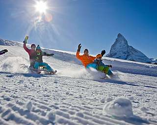 Gruppe von Menschen beim Schlittenfahren mit Berg im Hintergrund.