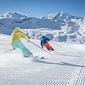 Zwei Skifahrer fahren auf einer präparierten Piste in den Bergen.