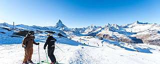 Deux skieurs se tiennent sur une piste enneigée avec vue sur la montagne.