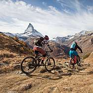 Zwei Mountainbiker fahren durch eine alpine Landschaft mit dem Matterhorn im Hintergrund.