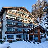 Ein Hotelgebäude im Schnee mit Balkonen und umgebenden Bäumen.