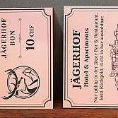 Zwei aufgestellte Karten mit Jägerhof-Logo und Hotelinformationen auf einer Holzfläche, daneben weitere Karten und Geweihdekor