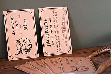Two vintage-style hotel cards with decorative borders and deer logo, standing on a wooden surface.