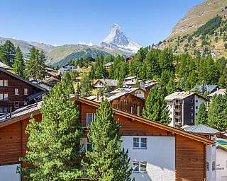 Alpenort mit Holzhäusern, Bäumen und Matterhorn im Hintergrund.