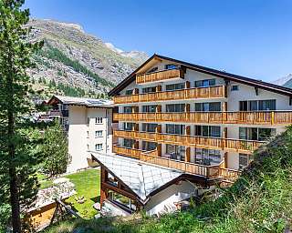 Mehrstöckiges Hotel mit Holzbalustraden in den Alpen bei klarem Himmel