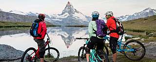 Drei Mountainbiker genießen die Aussicht auf die Berge und den See.