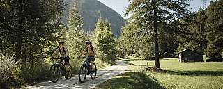 Zwei Personen fahren mit Fahrrädern auf einem schmalen Weg durch die Natur.