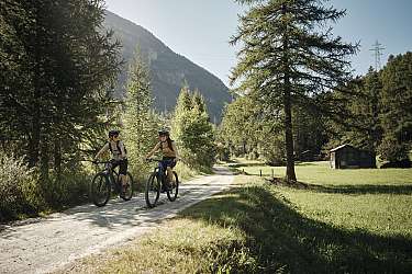 Two people riding mountain bikes on a gravel path through nature.