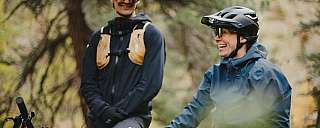Zwei Personen in Mountainbike-Ausrüstung lachen im Wald.
