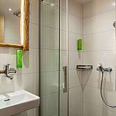 Helles Badezimmer mit Dusche, Waschbecken und Holzspiegel.