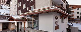View of a modern mountain cabin with snow and wooden cladding.