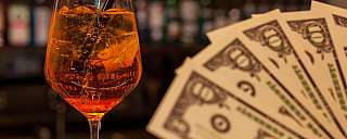 Ein Glas mit einem orangefarbenen Cocktail und Geldscheinen im Vordergrund.