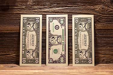 Three decorative dollar notes from the Jägerhof Hotel on a wooden surface.