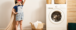 Ein Kind in einem Superheldenkostüm steht neben einer Waschmaschine.