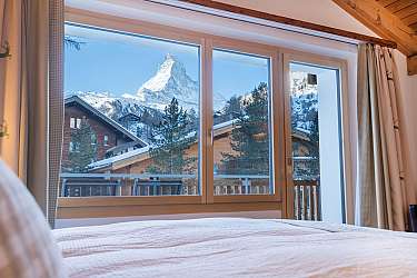 Blick aus einem Schlafzimmerfenster auf das schneebedeckte Matterhorn und Holzhäuser