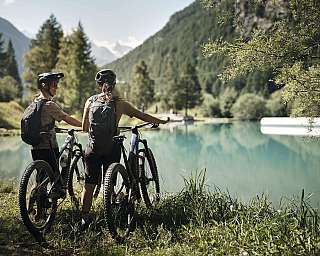 Two people with bicycles are standing by the calm lake.