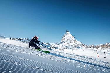 Skifahrer fährt auf präparierter Piste mit Matterhorn im Hintergrund bei klarem Himmel
