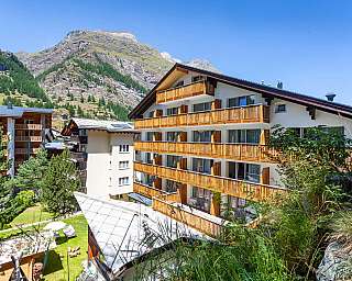 Modern hotel building with balconies and mountain landscape in the background.