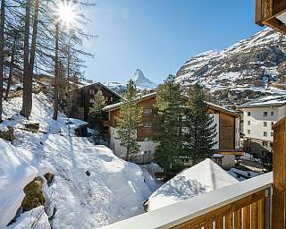 Blick auf schneebedeckte Häuser und Bäume mit Matterhorn im Hintergrund bei Sonnenschein