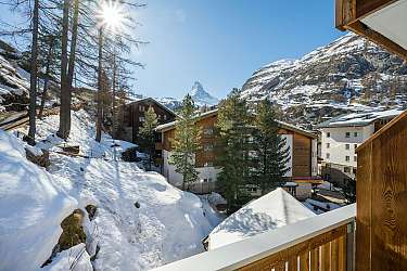 Schneebedeckte Chalets in einer alpinen Landschaft mit Bergen und blauem Himmel.