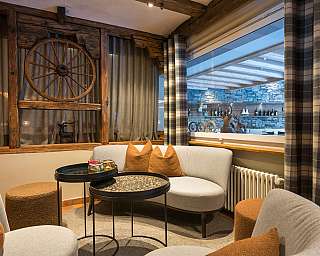 Sitzecke mit grauen Sesseln, braunen Kissen, Holzwanddeko und Fenster mit Blick auf Steinwand