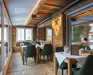 Gemütliches Restaurant mit Holzboden, grünen Stühlen, weißen Tischdecken und Hirschkopfbeleuchtung