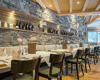 Langer Tisch mit gedeckten Plätzen, Steinwand, Holzdecke und Weinflaschenregal