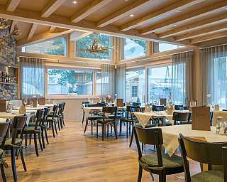 Restaurant mit Holzbalkendecke, Steinsäule, gedeckten Tischen und großen Fenstern