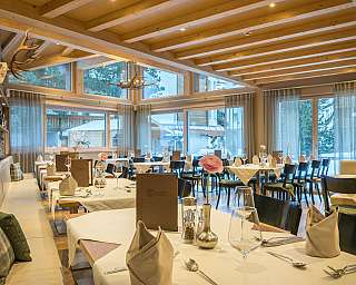 Restaurant mit Holzbalkendecke, gedeckten Tischen und großen Fenstern mit Blick nach draußen