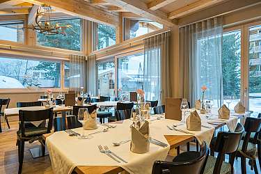 Restaurant mit gedeckten Tischen, Holzdecke und großen Fenstern mit Blick auf verschneite Landschaft