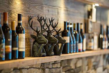 Regal mit Weinflaschen und drei Hirschfiguren aus Holz an einer Wand