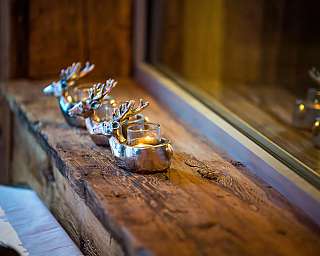 Drei silberne Kerzenhalter in Hirschform auf einem rustikalen Holztisch