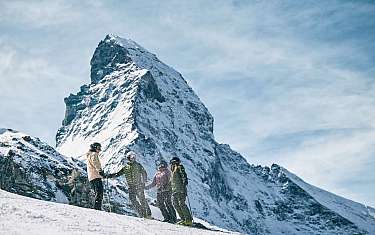 Vier Skifahrer stehen im Schnee vor dem schneebedeckten Matterhorn
