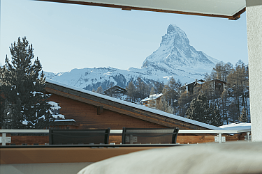 Panorama mit schneebedecktem Matterhorn und Holzhäusern.