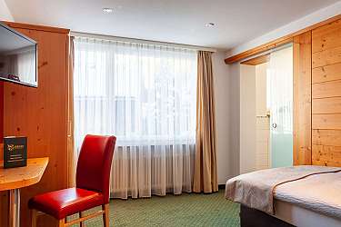 Gemütliches Hotelzimmer mit rotem Stuhl und Fenster mit Vorhängen.