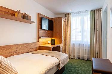 Ein helles Zimmer mit einem Einzelbett, Schreibtisch und Fernseher.