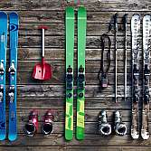 Verschiedene Skier, Skischuhe und eine Schaufel auf Holzboden.